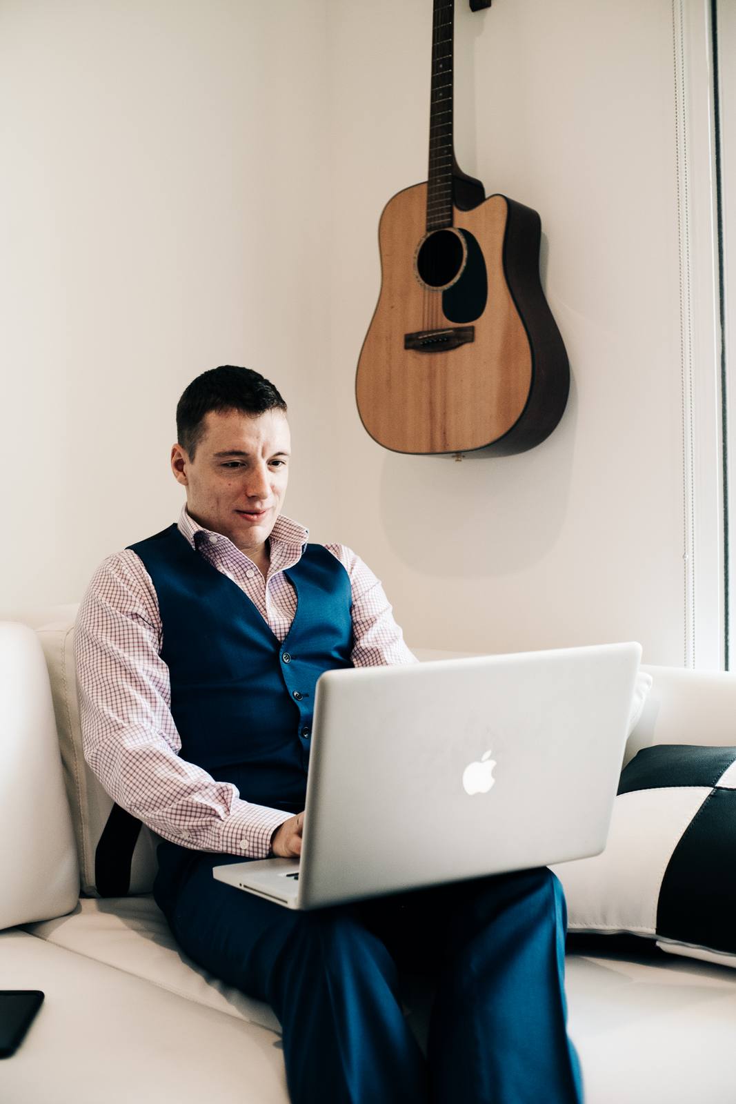 Mikhail on a white sofa with a laptop, a guitar on the wall